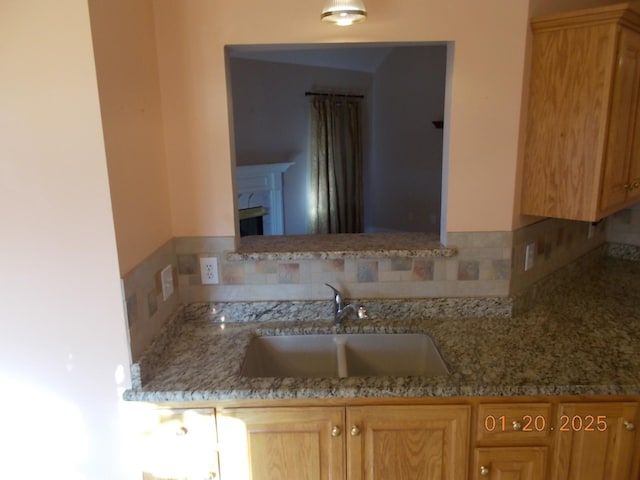 kitchen with a fireplace, backsplash, light stone counters, and sink