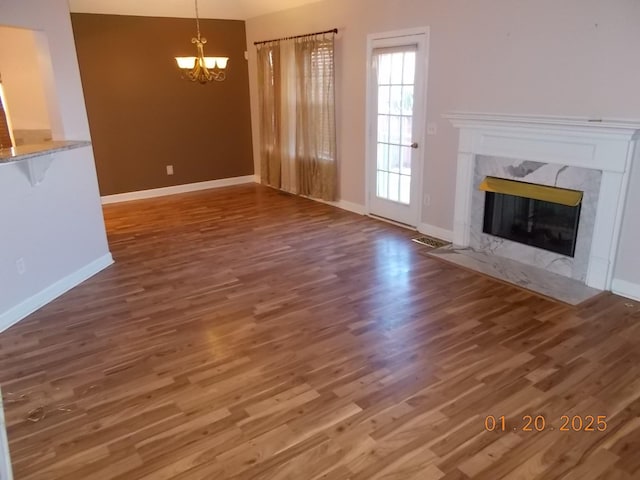 unfurnished living room featuring dark wood-type flooring, a high end fireplace, and a notable chandelier