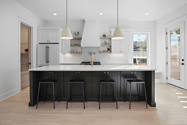 kitchen with premium range hood, high end fridge, hanging light fixtures, light hardwood / wood-style floors, and white cabinets