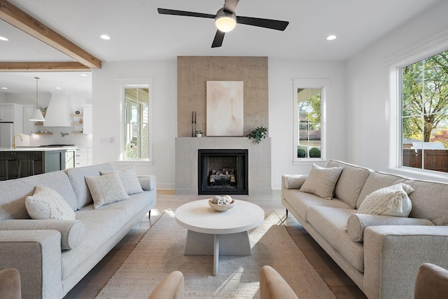 living room featuring sink, hardwood / wood-style flooring, ceiling fan, a fireplace, and beamed ceiling