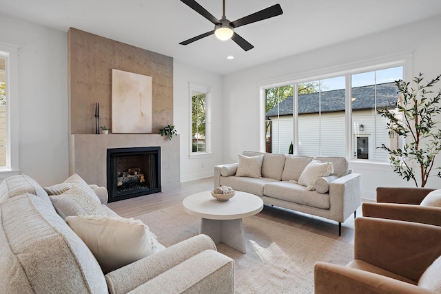 living room featuring ceiling fan, a large fireplace, and light hardwood / wood-style flooring