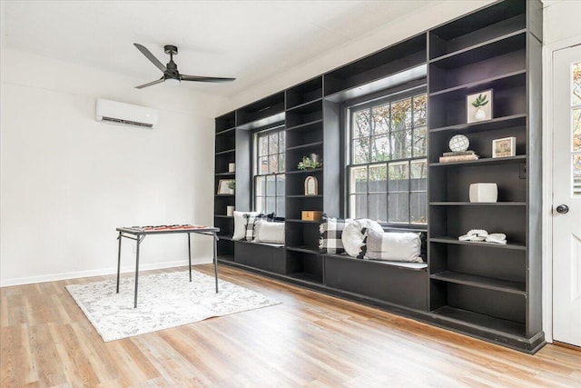 interior space featuring a wall mounted air conditioner, light hardwood / wood-style flooring, built in features, and ceiling fan