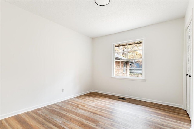 spare room with a textured ceiling and light hardwood / wood-style floors