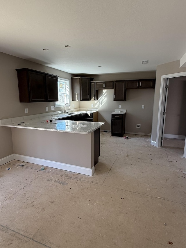 kitchen featuring light stone countertops, sink, dark brown cabinetry, and kitchen peninsula