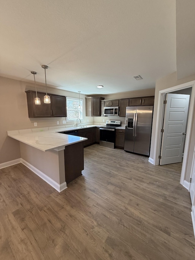 kitchen featuring wood finished floors, visible vents, a peninsula, dark brown cabinetry, and appliances with stainless steel finishes