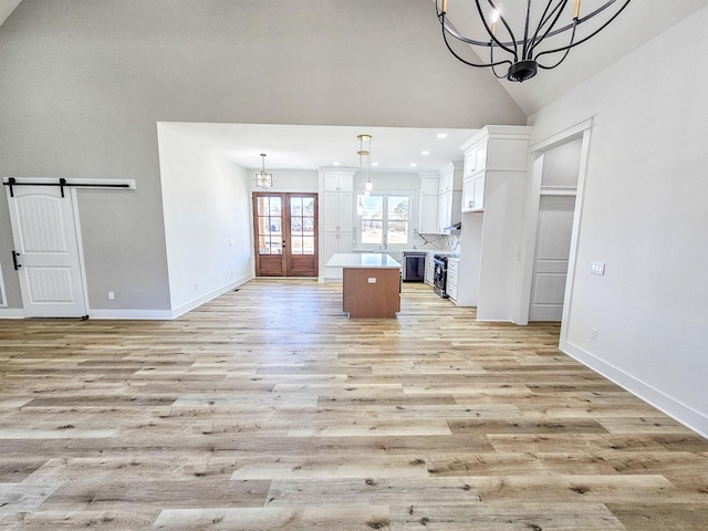 unfurnished living room with light wood-type flooring, a barn door, french doors, and high vaulted ceiling