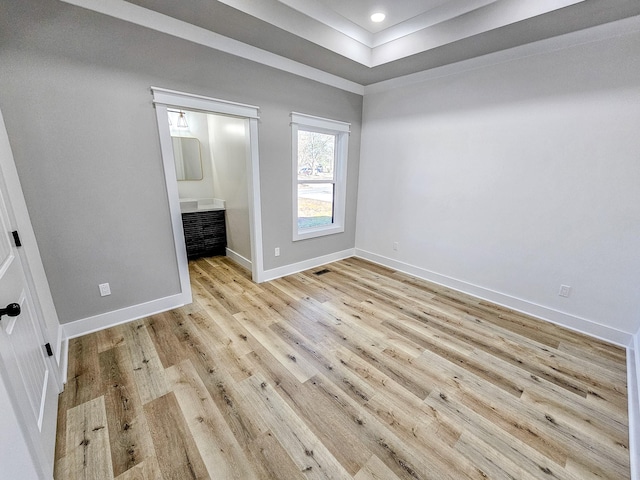 unfurnished bedroom featuring ensuite bathroom, a raised ceiling, and light wood-type flooring