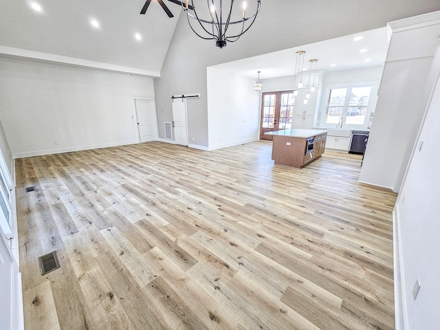 unfurnished living room with sink, a barn door, light hardwood / wood-style flooring, and high vaulted ceiling