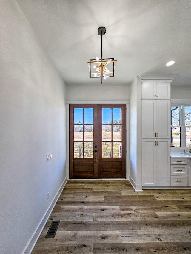 doorway to outside with french doors, an inviting chandelier, a wealth of natural light, and wood-type flooring