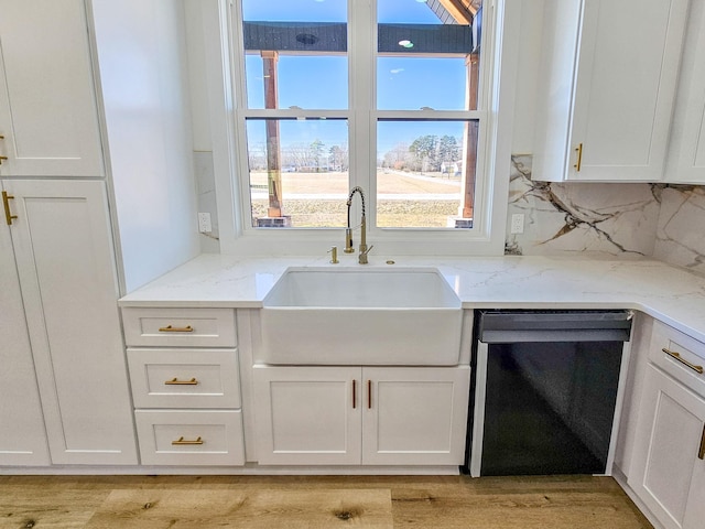 kitchen with decorative backsplash, sink, black dishwasher, and white cabinetry