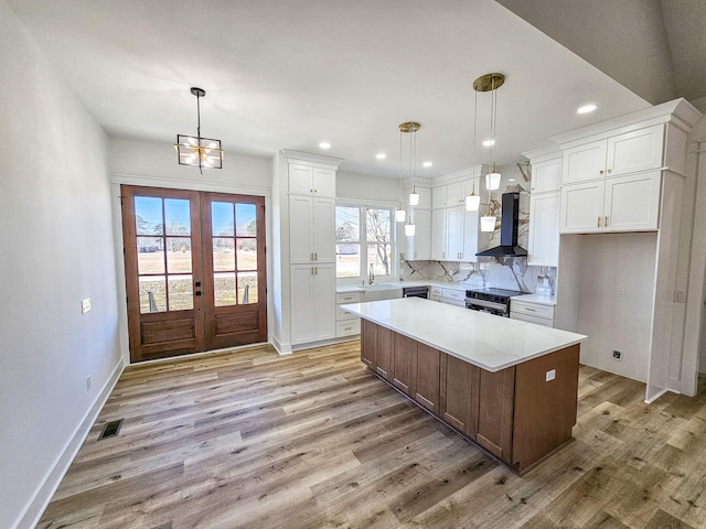 kitchen with electric range, white cabinetry, wall chimney range hood, and a kitchen island