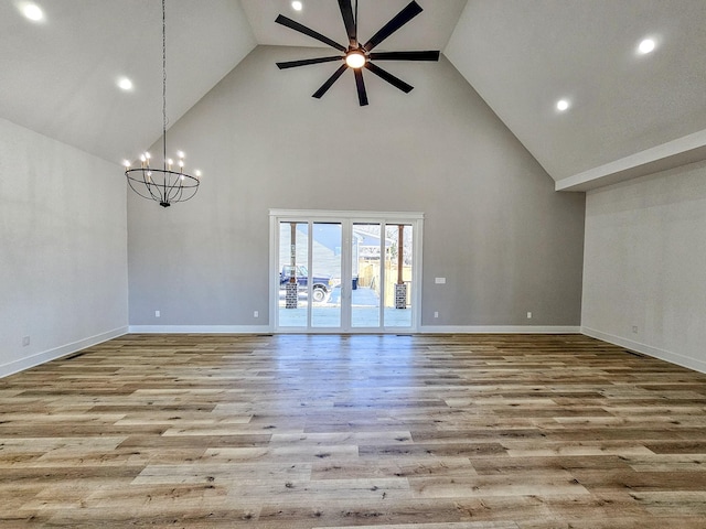 unfurnished living room with light wood-type flooring, ceiling fan with notable chandelier, and high vaulted ceiling