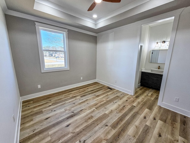 empty room featuring ceiling fan, light hardwood / wood-style flooring, and a tray ceiling