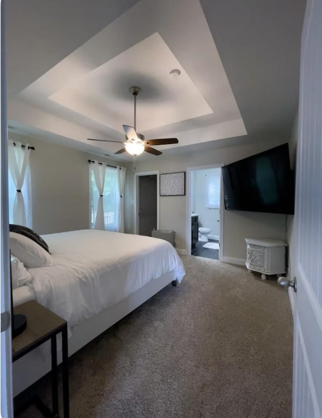 bedroom with ceiling fan, carpet, a tray ceiling, and ensuite bathroom