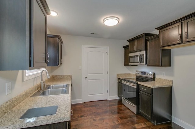 kitchen with sink, dark wood-type flooring, stainless steel appliances, dark brown cabinets, and light stone counters