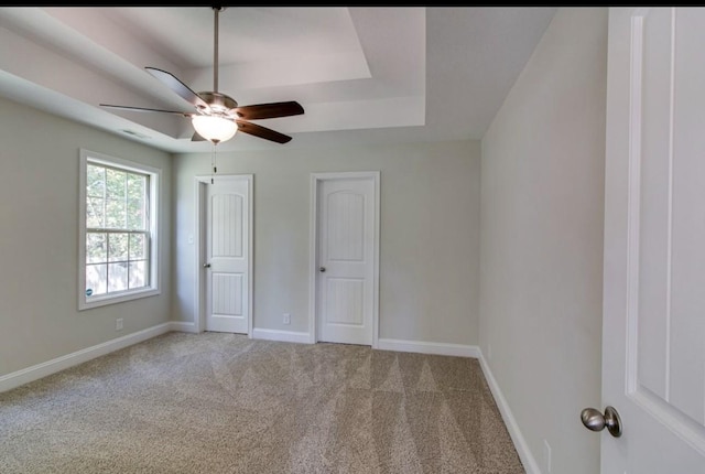 unfurnished bedroom with ceiling fan, light carpet, and a tray ceiling