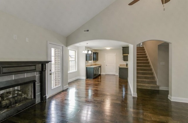 unfurnished living room with ceiling fan, dark hardwood / wood-style floors, a tile fireplace, and high vaulted ceiling