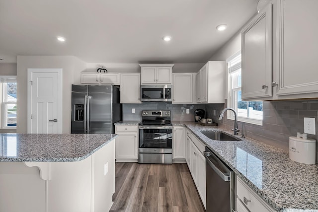 kitchen featuring light stone countertops, white cabinets, appliances with stainless steel finishes, sink, and a breakfast bar area