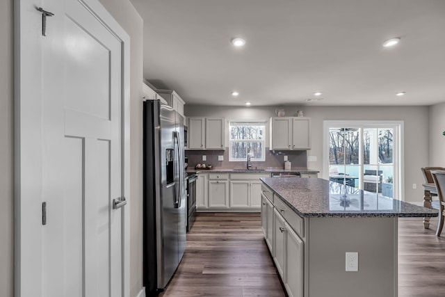 kitchen featuring appliances with stainless steel finishes, tasteful backsplash, a center island, dark stone countertops, and sink