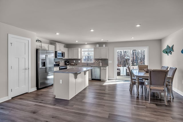 kitchen featuring appliances with stainless steel finishes, dark hardwood / wood-style flooring, dark stone counters, white cabinets, and a center island