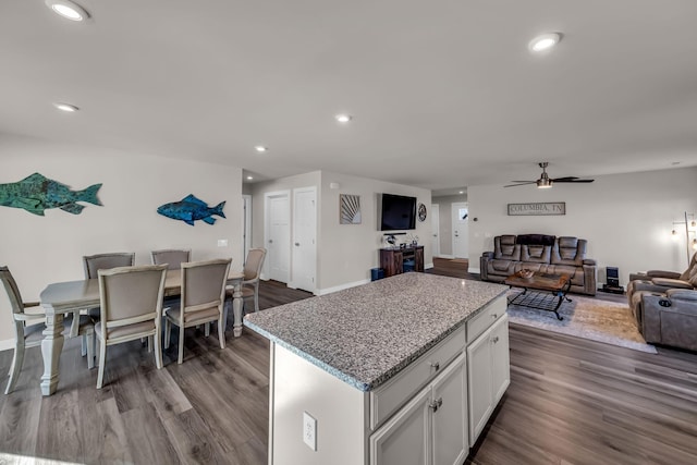 kitchen with ceiling fan, a kitchen island, hardwood / wood-style flooring, light stone countertops, and white cabinets