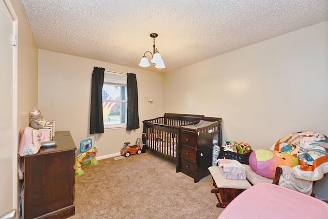 bedroom with light colored carpet, a textured ceiling, a nursery area, and a notable chandelier