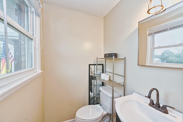 bathroom with toilet, a healthy amount of sunlight, sink, and a textured ceiling