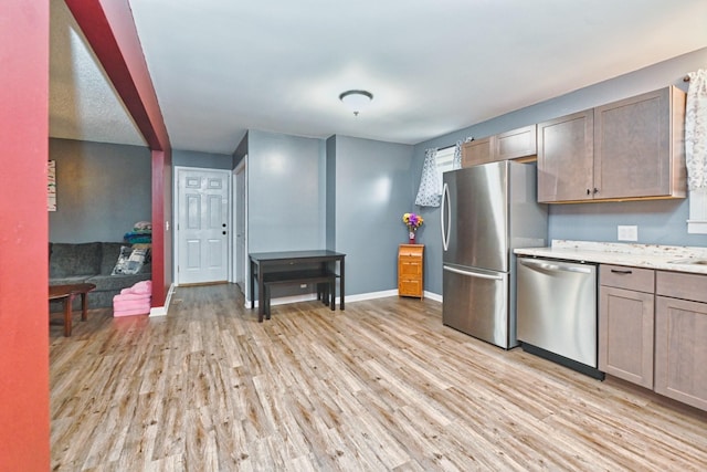 kitchen with appliances with stainless steel finishes, light hardwood / wood-style floors, and light stone counters