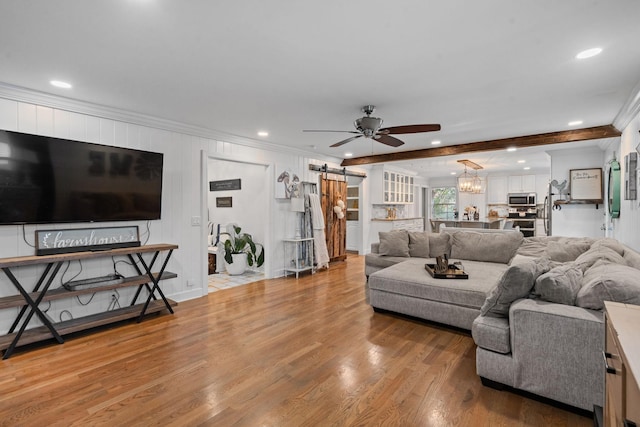 living room with ceiling fan with notable chandelier, hardwood / wood-style floors, beamed ceiling, crown molding, and a barn door