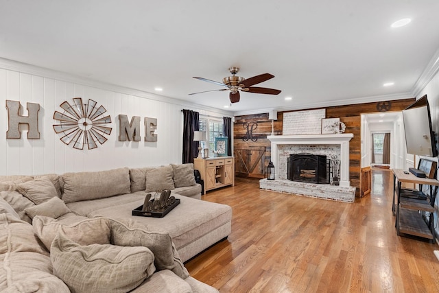 living room featuring hardwood / wood-style floors, wooden walls, a brick fireplace, ceiling fan, and crown molding