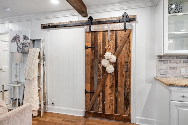 details featuring beam ceiling, a barn door, wood-type flooring, and ornamental molding