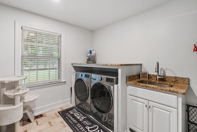 clothes washing area featuring washing machine and dryer, sink, and cabinets