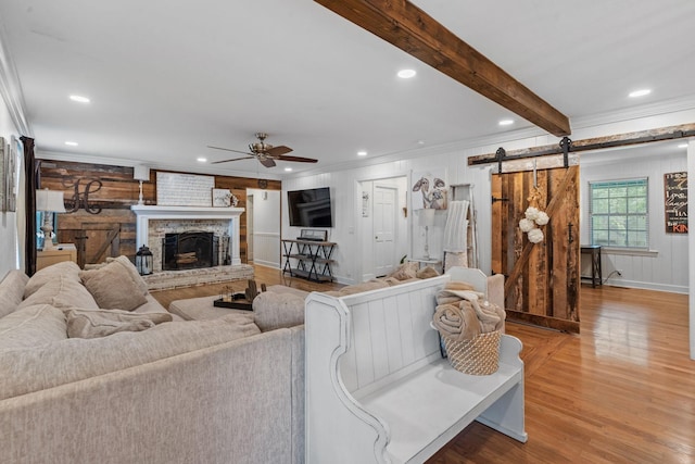 living room with beamed ceiling, ceiling fan, hardwood / wood-style flooring, crown molding, and a barn door