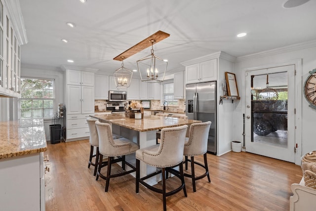 kitchen with stainless steel appliances, decorative light fixtures, white cabinets, light stone counters, and a center island