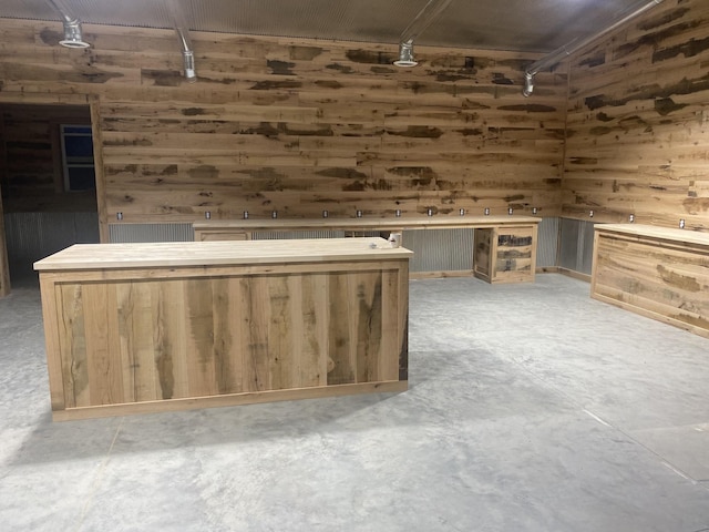 bar with light brown cabinets, wood walls, and concrete flooring