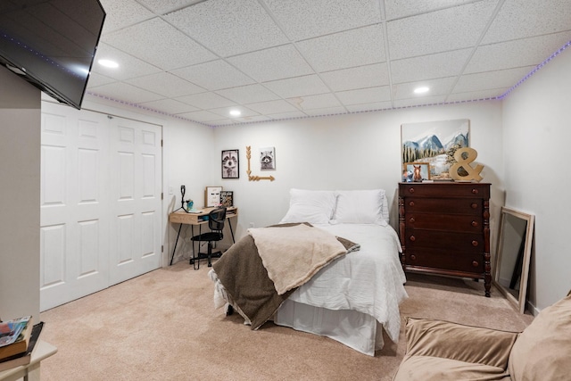 bedroom with light carpet, a drop ceiling, and a closet