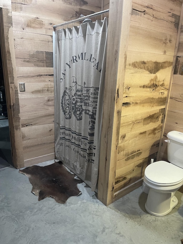 bathroom with toilet, concrete flooring, and wooden walls