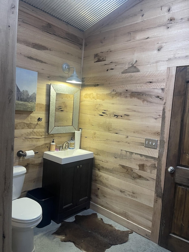 bathroom featuring toilet, vanity, and wooden walls