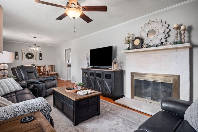 living room featuring light wood-type flooring, ceiling fan with notable chandelier, crown molding, and a textured ceiling