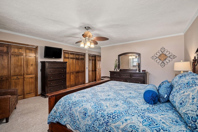 bedroom with a textured ceiling, ceiling fan, light colored carpet, crown molding, and multiple closets