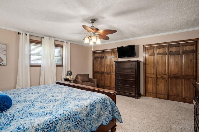 bedroom featuring a textured ceiling, two closets, ceiling fan, light colored carpet, and crown molding