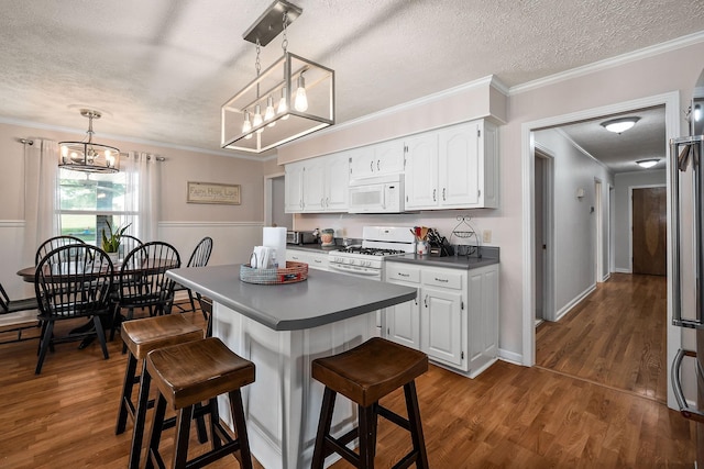 kitchen featuring decorative light fixtures, a breakfast bar, white appliances, white cabinetry, and a textured ceiling