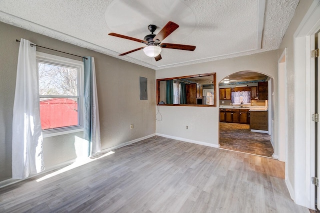 unfurnished living room with a textured ceiling, sink, ceiling fan, electric panel, and light hardwood / wood-style flooring