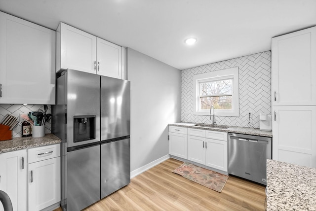 kitchen featuring white cabinetry, stainless steel appliances, tasteful backsplash, light stone counters, and sink