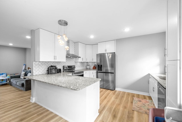 kitchen with white cabinetry, kitchen peninsula, appliances with stainless steel finishes, wall chimney range hood, and pendant lighting