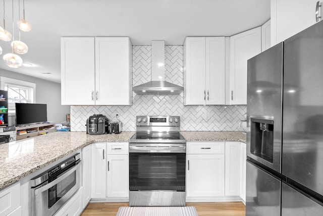 kitchen featuring stainless steel appliances, decorative backsplash, white cabinets, and wall chimney range hood