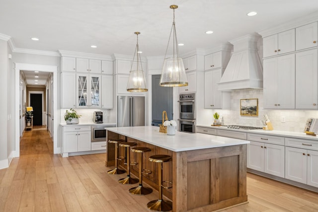 kitchen featuring white cabinetry, appliances with stainless steel finishes, a center island with sink, and custom range hood