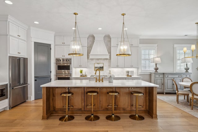 kitchen with decorative light fixtures, an island with sink, stainless steel appliances, and white cabinetry