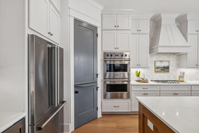 kitchen featuring decorative backsplash, white cabinetry, appliances with stainless steel finishes, and custom exhaust hood