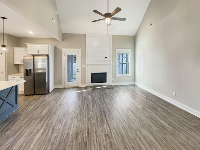 unfurnished living room featuring ceiling fan, a large fireplace, dark hardwood / wood-style floors, and lofted ceiling with beams